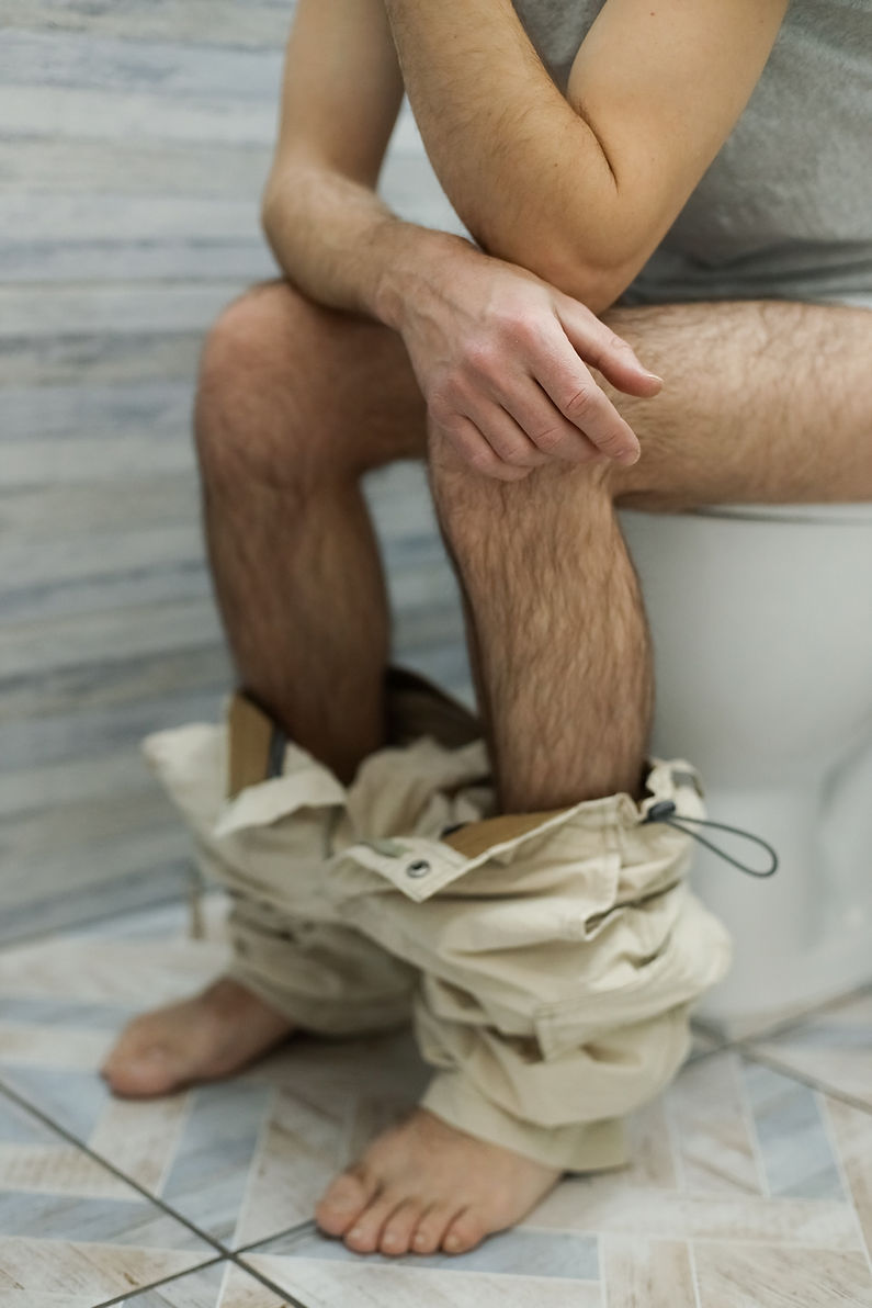 A man with his pants down is sitting on the toilet.jpg