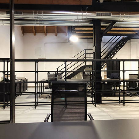 Scorcio del nostro studio-showroom. Scrivanie con poltrone, mobili contenitori, libreria. Scala che porta al soppalco dove si trova l'ufficio amministrativo e marketing. Tutte le strutture sono realizzate in carpenteria color grigio antracite