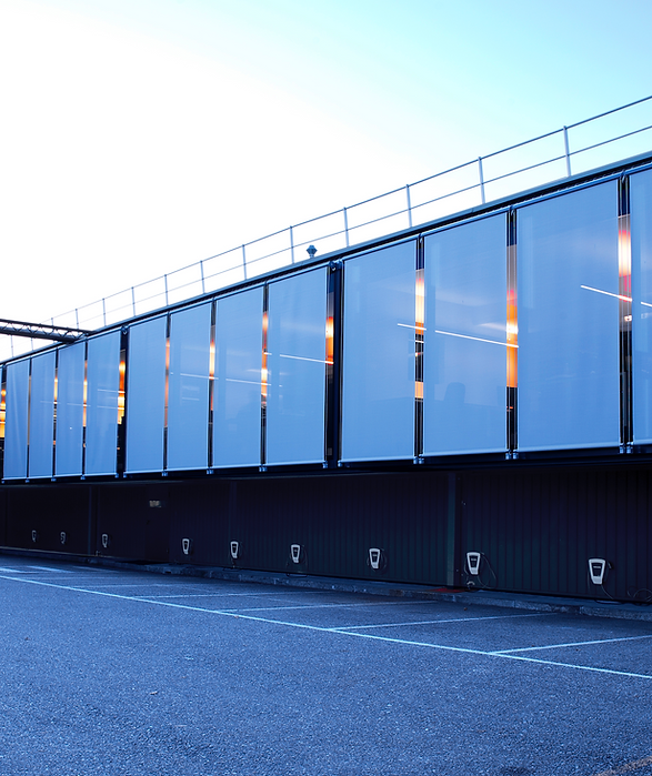 Il grande parallelepipedo sospeso è una lunga facciata continua, non apribile. La struttura integra le tende a caduta verticale per proteggere l'interno degli uffici dalla luce naturale. In questa foto tutte le tende sono abbassate