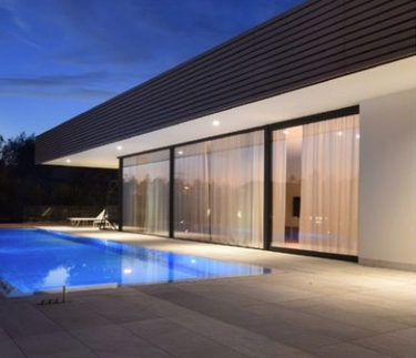 Serramento scorrevole in alluminio composto da tre sezioni installato fronte piscina. Il colore del serramento è nero come il rivestimento di tutti perimetro frontale della struttura della copertura della villa