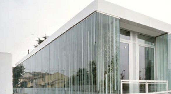 dettaglio della parte più alta dell'edificio. In primo piano c'è l'angolo che inontra la facciata frontale e quella laterale. La struttura portante è in metallo color bianco. Le facciate ventilate in vetro sono serigrafate con linee verticali 