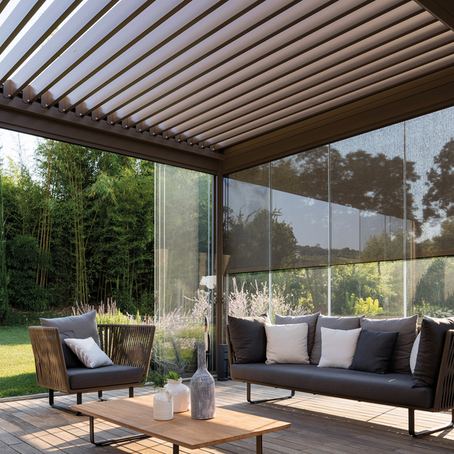 Pergola bioclimatica con lame orientabili. La chiusura perimetrale è composta da vetrate scorrevoli e da teli Raso ombreggianti. La copertura è formata da lame orientabili. La pergola bioclimatica è installata in un giardino, ma è addossata alla casa