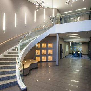 Modern corporate staircase with glass railing, wood flooring, and decorative pendant lighting.