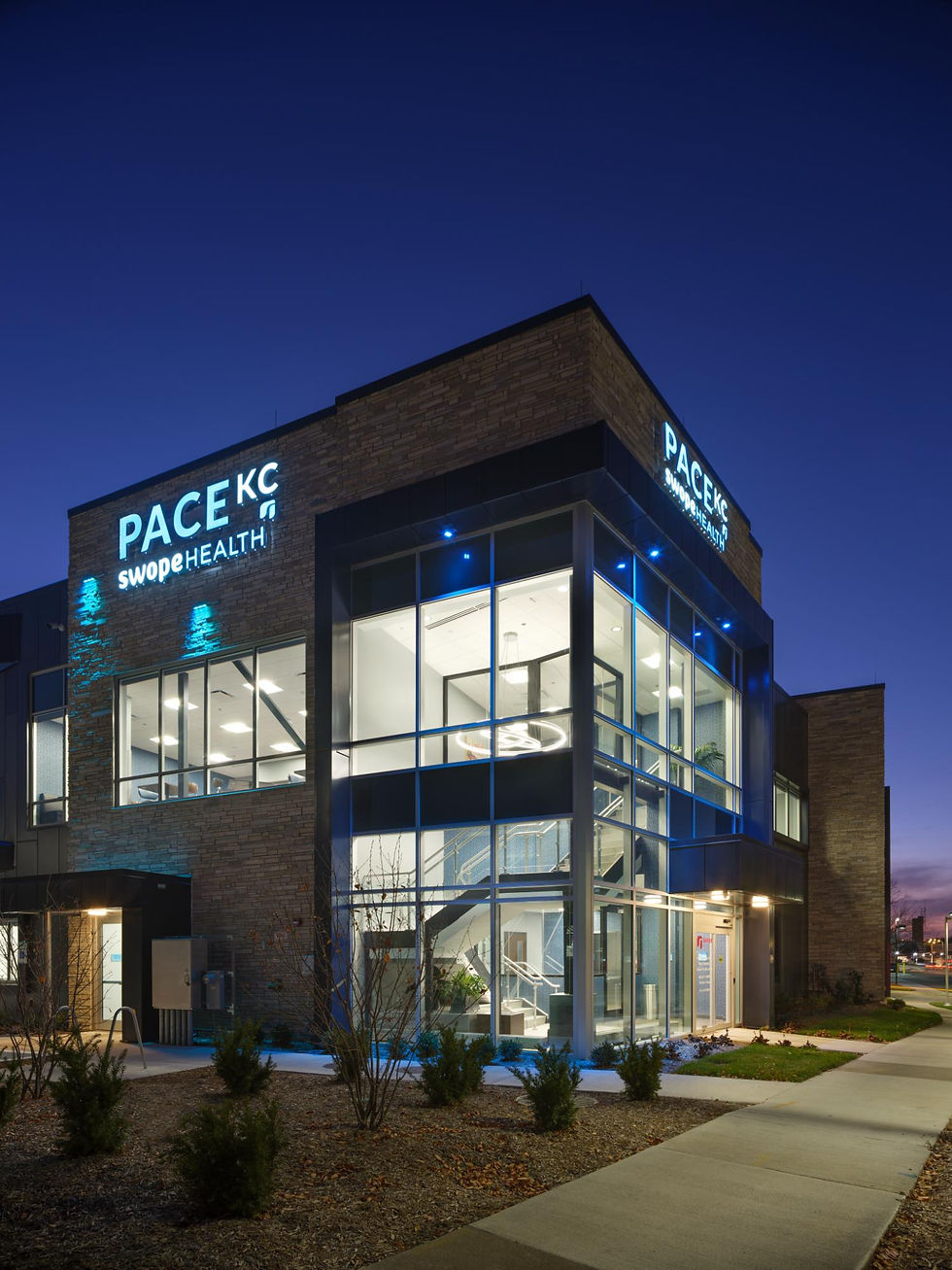 The PACE KC Adult Wellness Center illuminated at dusk, highlighting contemporary architecture, expansive glazing, and illuminated signage along Dr. Martin Luther King Jr. Boulevard.