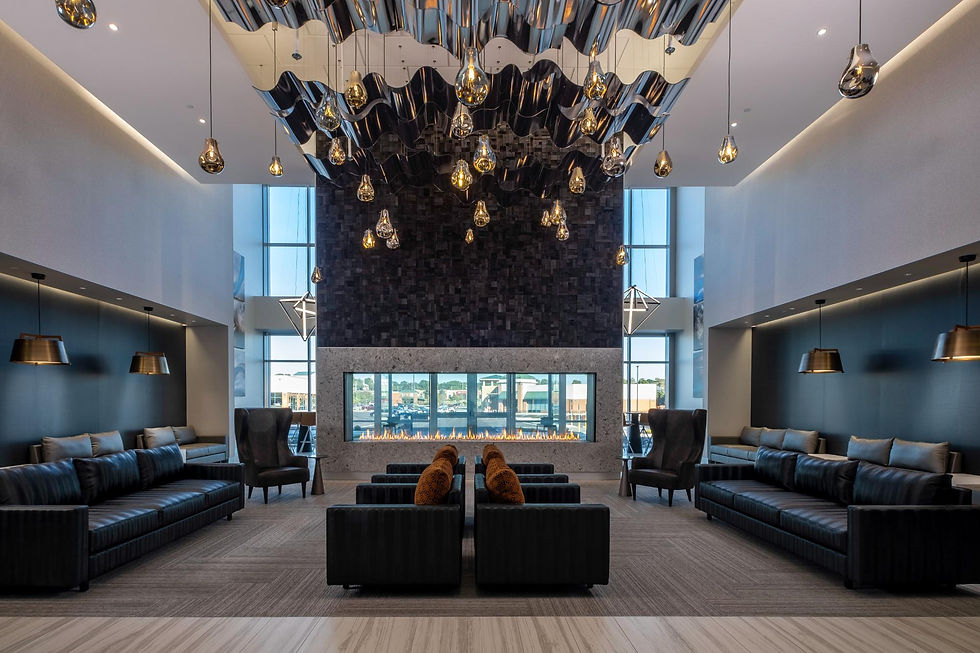 Modern lobby featuring a dramatic floor-to-ceiling fireplace clad in textured stone, soaring ceilings, contemporary furnishings, and abundant natural daylight.