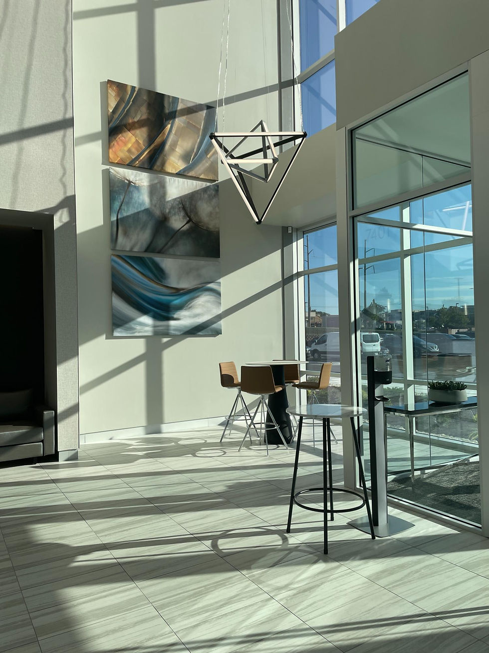 Sunlit lobby seating area with floor-to-ceiling glass, abstract artwork, contemporary pendant lighting, and casual meeting tables in a modern medical research facility.