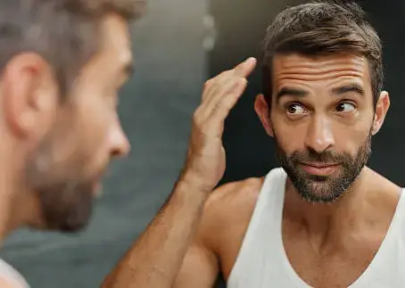 middle aged man looking and cleaning up look in bathroom mirror