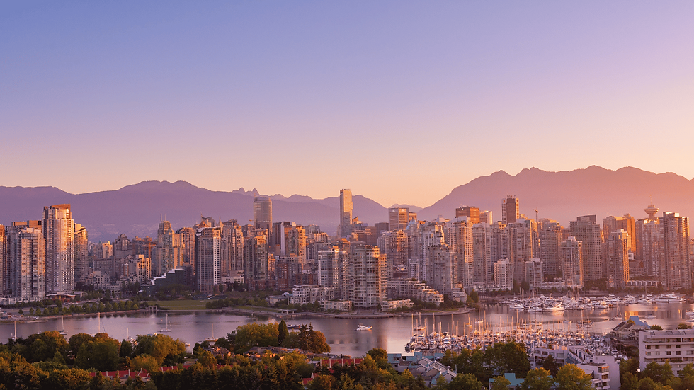 View of Vancouver, BC Canada at sunset with the harbour, city buildings visible in the foreground. Dark purple mountains rise above the city in the background.