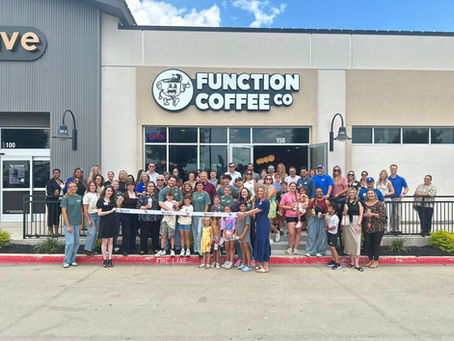 A group of people in front of a coffee shop for a ribbon cutting.