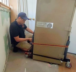 Worker securing a tall gray safe on a wheeled moving platform with straps.