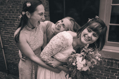 Bruid knuffelt met bruidsmeisjes in een ongedwongen trouwfoto in zwartwit.