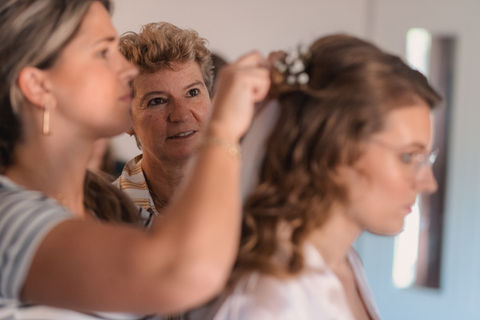 De moeder van de bruid kijkt vol bewondering naar haar dochter die wordt opgemaakt voor haar trouwerij. De fotograaf legt alle details vast bij deze bruiloft in Lisse.