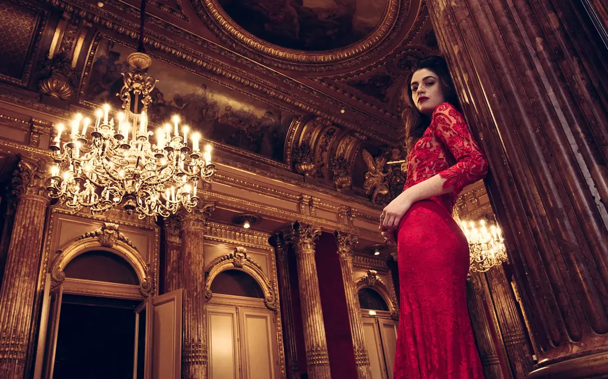 Model in red evening dress under chandelier in theater-like space