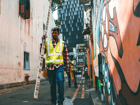 Singapore construction worker in safety vests walk down a narrow, colorful mural-lined alley with equipment.