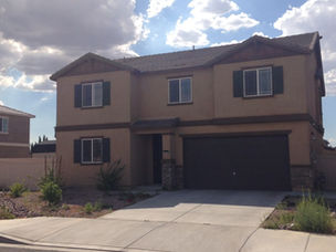 Two-story stucco home with dark shutters, tile roof, and a two-car garage in a Lancaster, California neighborhood with desert landscaping
