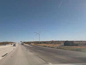 Northbound State Route 14 passing Lake Palmdale in the Antelope Valley, with open high desert and mountains in the distance under a clear blue sky.