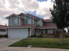 Two-story home in Lancaster, CA with sage green exterior, white trim, tile roof, and attached two-car garage