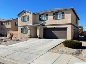 Two-story stucco home in Lancaster, California, with a two-car garage, tile roof, and low-water desert landscaping under a clear blue sky.