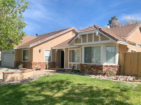 Single-story single-family home in Palmdale, California, with a tile roof, brick accents, and a green front lawn under a clear blue sky.