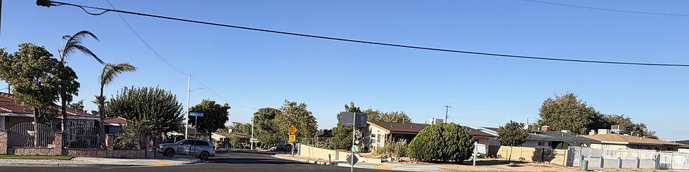 Quiet residential corner of older single-story tract homes with mature trees and palms in West Palmdale, California.