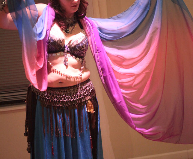 Ember Dragon is doing a snake like movement. She has a blue and pink veil over her shoulders. She looks serene.