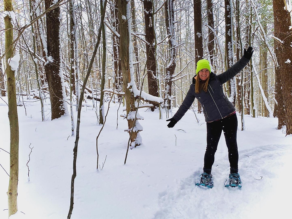 Woman walking through snowy forest wearing snowshoes.