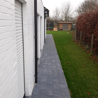 zijpad in grijze betonklinkers langs woning