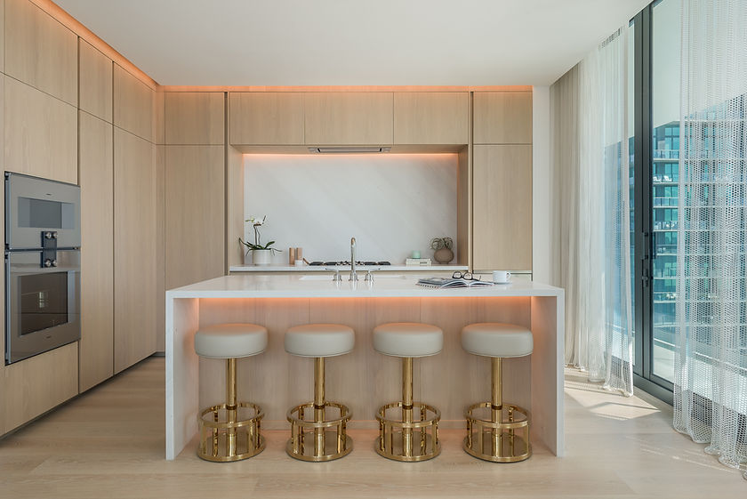 Kitchen at The Tampa EDITION with pale wood cabinetry, a stone island and four gold-base stools.