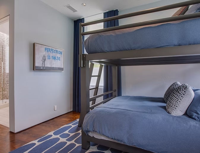Wood bunk beds with blue bedding beside a blue patterned rug and framed artwork.