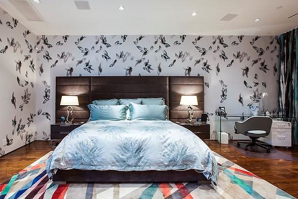 Contemporary bedroom with butterfly-patterned wallpaper, blue bedding and a geometric multicolor rug.
