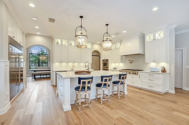 White farmhouse kitchen with a paneled island, blue upholstered counter stools and glass pendant lighting.