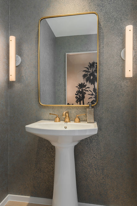 Powder room at The Tampa EDITION with a gold-framed mirror, wall sconces and pedestal sink.