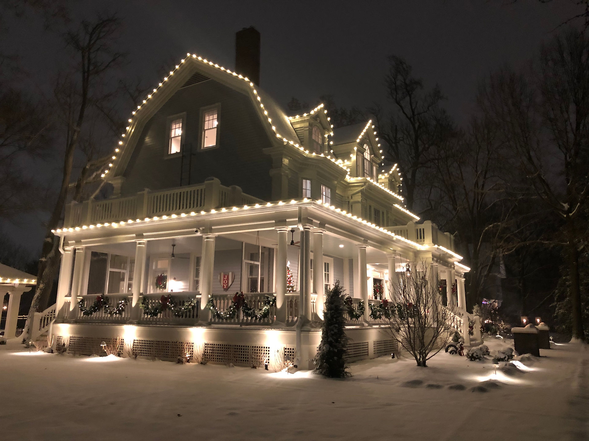 A blanket of snow covers the yard in elegant silence with white lights all over the house giving everything a wintery glow.