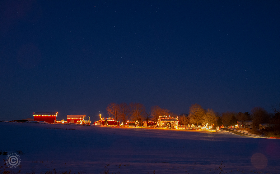 A Country Christmas farm with lights aglow in the night sky.