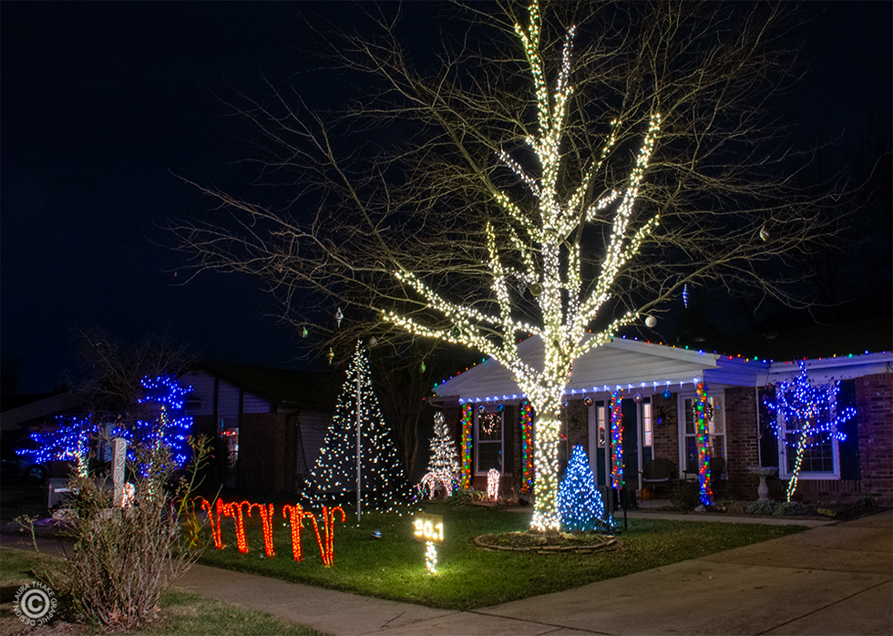 A tall tree wrapped in white lights with other lights on the house and yard.