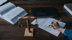 Person signing a legal document at a desk with a scale of justice and open books, representing contracts and legal decision-making