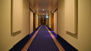 Empty hotel corridor with patterned carpet, closed room doors, and warm lighting leading to a vanishing point