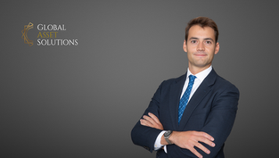 Portrait of a confident young man in a navy blue suit with folded arms, standing in front of a grey background with the Global Asset Solutions logo