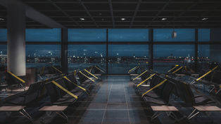 Empty airport waiting area with rows of seats blocked off, overlooking a dimly lit runway at night.