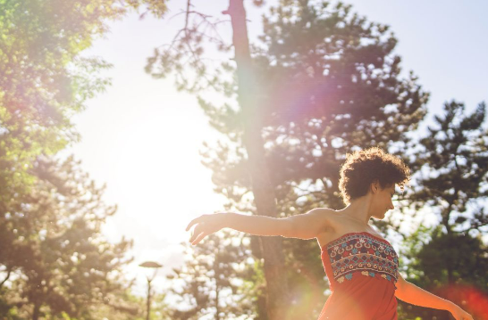 Mujer bailando en trance relajante en medio de un bosque iluminado por una luz clara del sol que inunda la escena. Parecido a lo que se vivirá en el retiro de Verano en Sanxenxo con Juan Magariños. Experiencias GranRURAL
