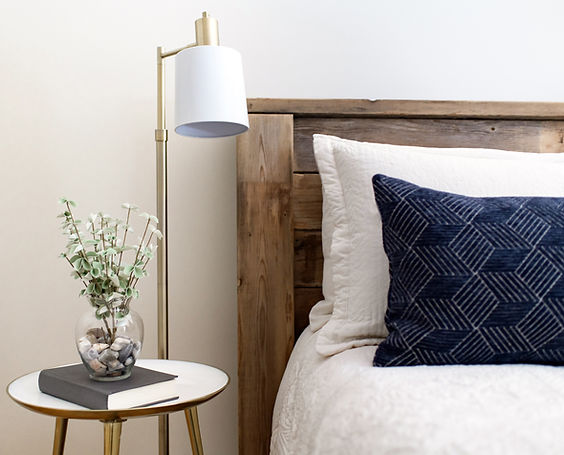 Rustic headboard and stylish white and navy bedding beside warm metal floor lamp