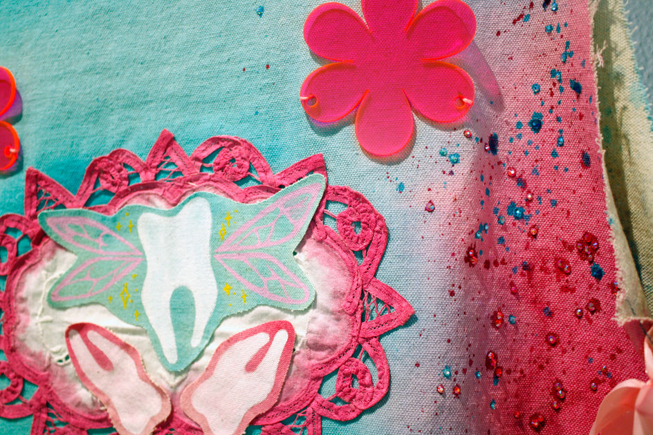 a close up of a blue and pink tunic displaying rhinestones and images of teeth layered on top of a doily 