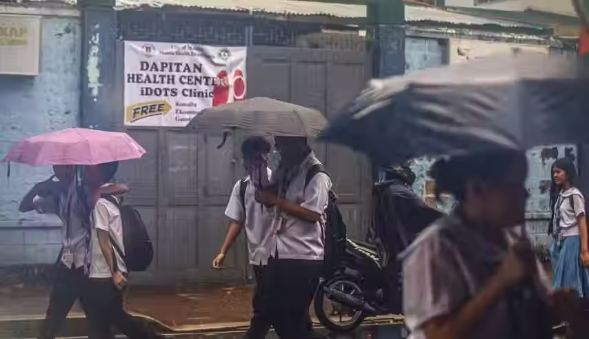 Hulagway sa mga estudyante nga naglakaw ilalom sa ulan samtang naggamit og mga payong sa gawas sa Dapitan Health Center.