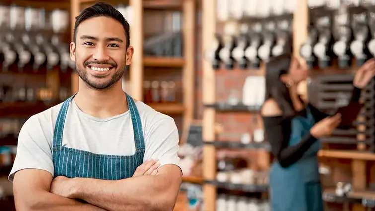 Latino shop owner proudly smiles while his female co-owner checks inventory