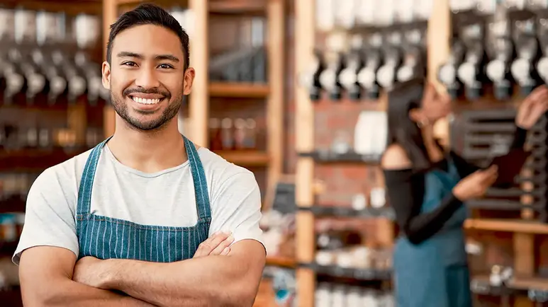 Latino shop owner proudly smiles while his female co-owner checks inventory
