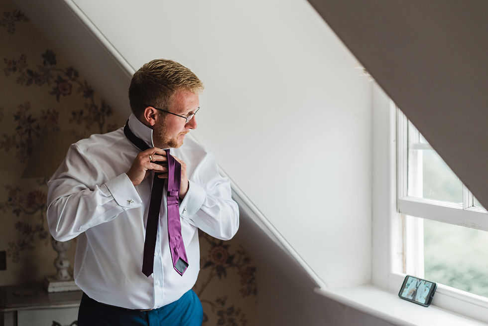 Groom learning how to tie his tie by watching a tutorial on his phone on the morning of his wedding at Pynes House, Exeter.