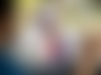 Girl in red striped shirt waves goodbye to a person in a car. She stands on a school path with a purple backpack, smiling under tree shade.