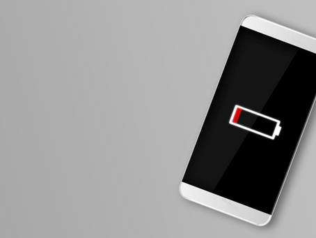 Smartphone with low battery icon on screen, black background. Set on light grey surface. Emphasizes urgency and need to recharge.