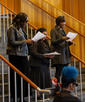 The side profiles of the Word Life Corral as they perform 'Get a Life'. All three of them hold up lyric sheets. At the bottom right of the picture is the back of Millicent's head, as well as the cello's scroll.