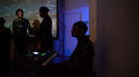 Jaz sits at her keyboard in the shadows, looking away from the camera. In the background and to her left, stand the shadowy forms of the Word Life Corral. The group are waiting for their cue to begin the second performance.